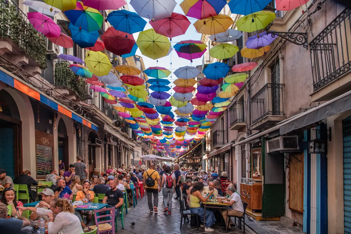 colorful umbrella hanging on a street full of restaurants in catania street food tour