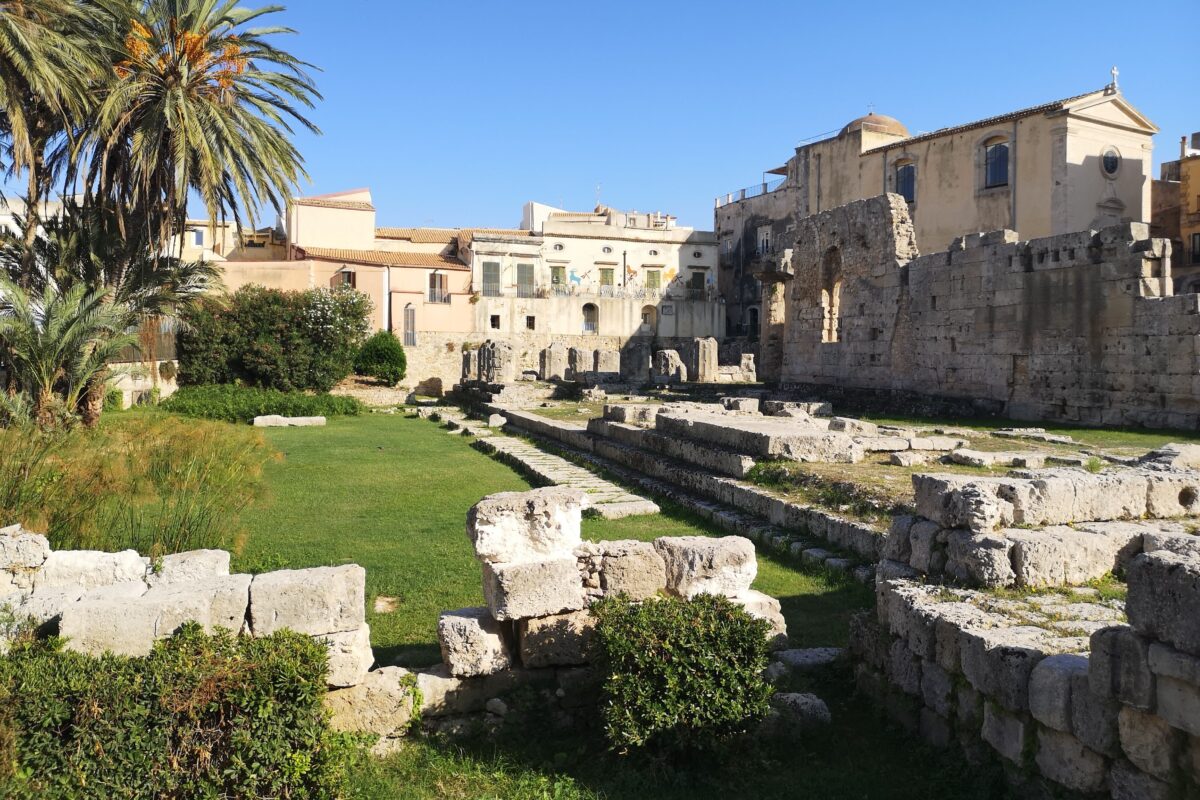 view of ruins of an old temple invaded by vegetation in the middle of a city temple of apollo on ortigia island