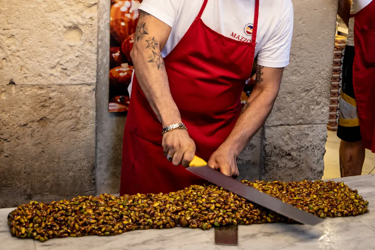hands cutting a long torrone made of pistachio and nuts torrone siciliano manufacturing in ortigia